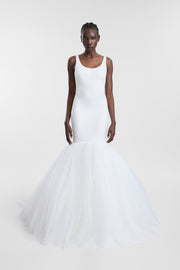 A model wearing an ivory scoop neck wedding gown with a fitted bodice and voluminous layered tulle trumpet skirt, photographed against a seamless light grey studio background.