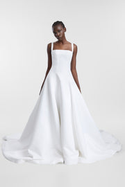 A model wearing an ivory satin wedding gown with a square neckline, corseted bodice and full A-line skirt, photographed against a seamless light grey studio background.