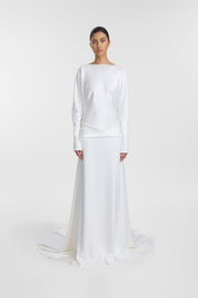 A model wearing an ivory long-sleeve satin wedding gown with a relaxed silhouette, open back and floor-length skirt, photographed against a seamless light grey studio background.