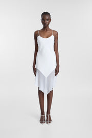 A model wearing an ivory midi dress with spaghetti straps, a scoop neckline and asymmetrical chiffon hem, photographed against a seamless light grey studio background.