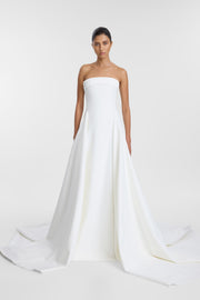 Model wearing the Mati ivory strapless A-line wedding gown with a straight neckline, cinched waist, side split and dramatic train.