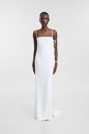 A model wearing an ivory maxi dress with fine satin straps, a straight neckline and side tie detailing, photographed against a seamless light grey studio background.