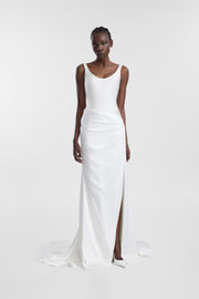 A model wearing an ivory satin wedding gown with a scoop neckline, asymmetrical draping and thigh-high side slit, photographed against a seamless light grey studio background.