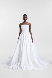 A model wearing an ivory full-length bridal skirt with gathered duchess satin, layered tulle and a sweeping train, photographed against a seamless light grey studio background.