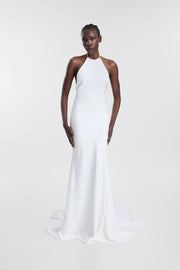Model wearing the Piero ivory halter wedding gown with a high neckline, open back, gold ring closure and streamlined silhouette.