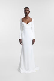 A model wearing an ivory long-sleeve wedding gown with a fitted silhouette, sweetheart neckline and floor-length skirt, photographed against a seamless light grey studio background.