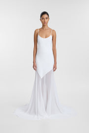 A model wearing an ivory scoop neck wedding gown with delicate straps, an asymmetrical hem and flowing chiffon train, photographed against a seamless light grey studio background.