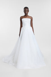A model wearing an ivory tulle bridal skirt with a satin waistband, voluminous silhouette and sweeping train, photographed against a seamless light grey studio background.