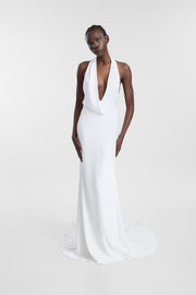 A model wearing an ivory halter neck wedding gown with a plunging neckline, fitted silhouette and gently flared skirt, photographed against a seamless light grey studio background.